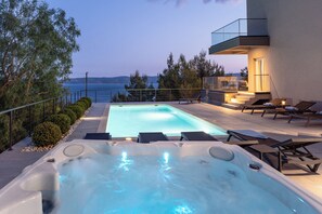 Uma área moderna com piscina ao ar livre, hidromassagem, espreguiçadeiras e vista para o mar.