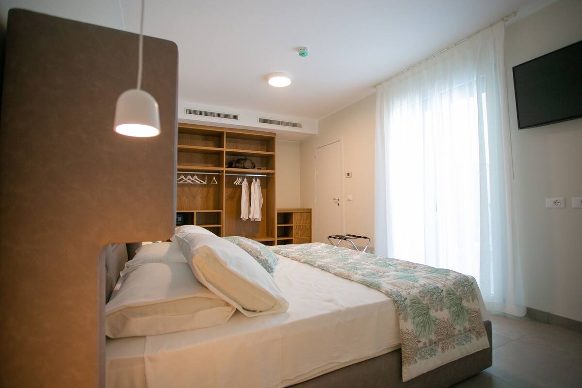 Une chambre à coucher avec un lit, une armoire, une télévision et une fenêtre avec des rideaux.