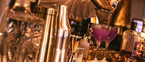 A bartender pouring a drink into a martini glass at a bar.