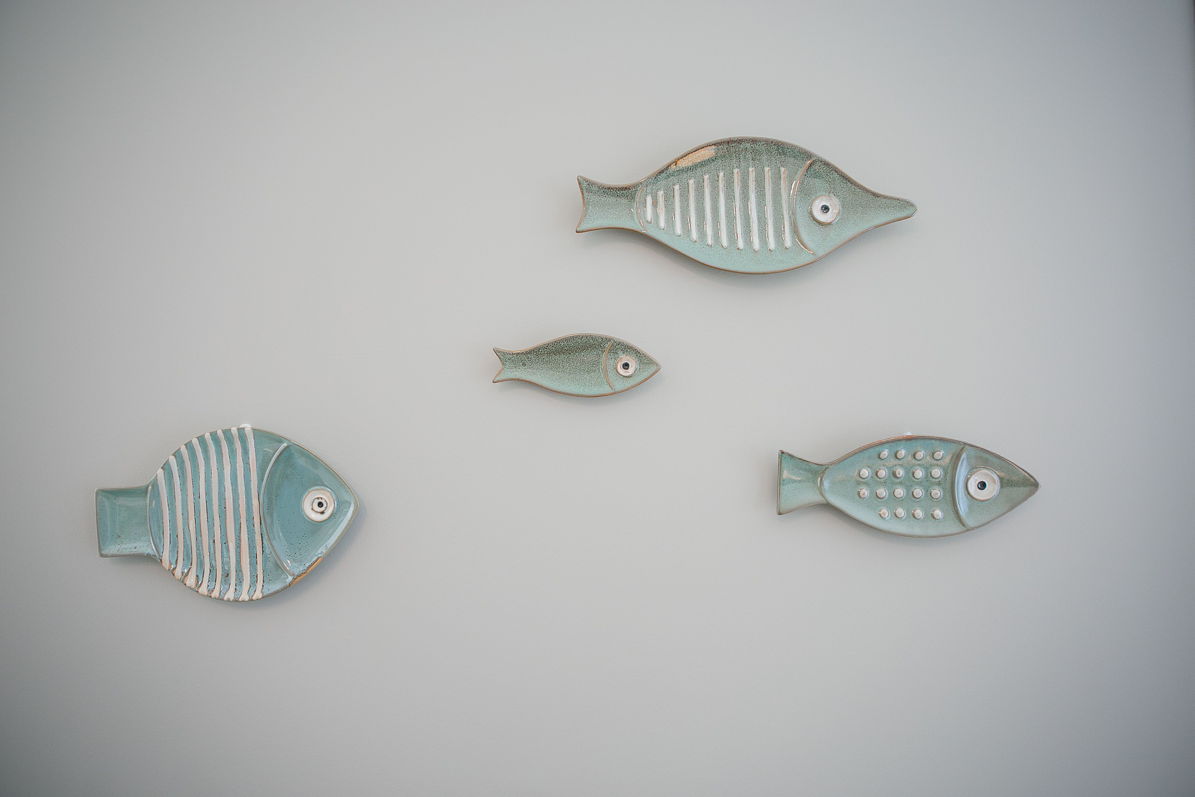 Four ceramic fish of varying sizes on a plain background.