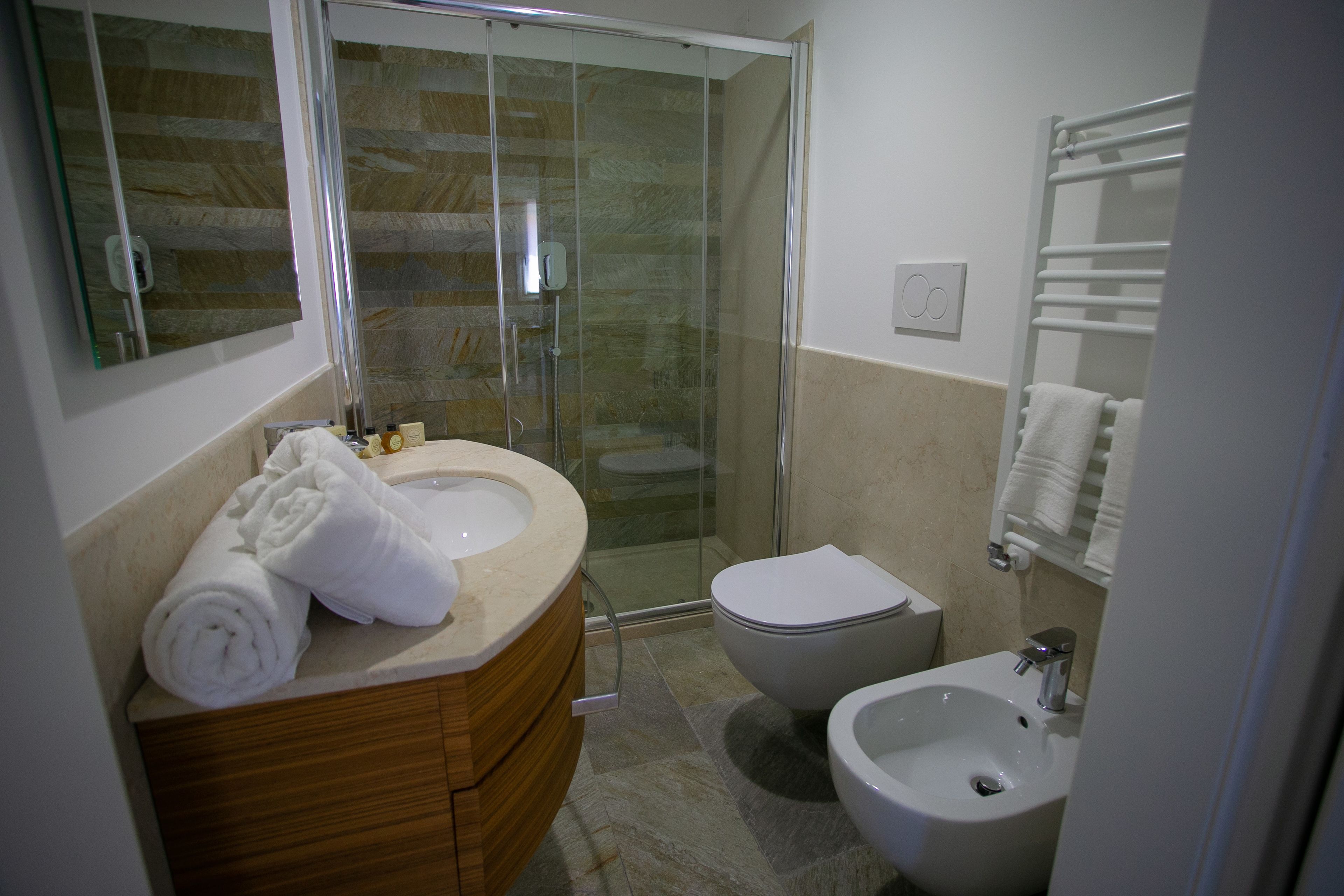 Un baño moderno con cabina de ducha de vidrio, tocador de madera, lavamanos blanco y un bidé.