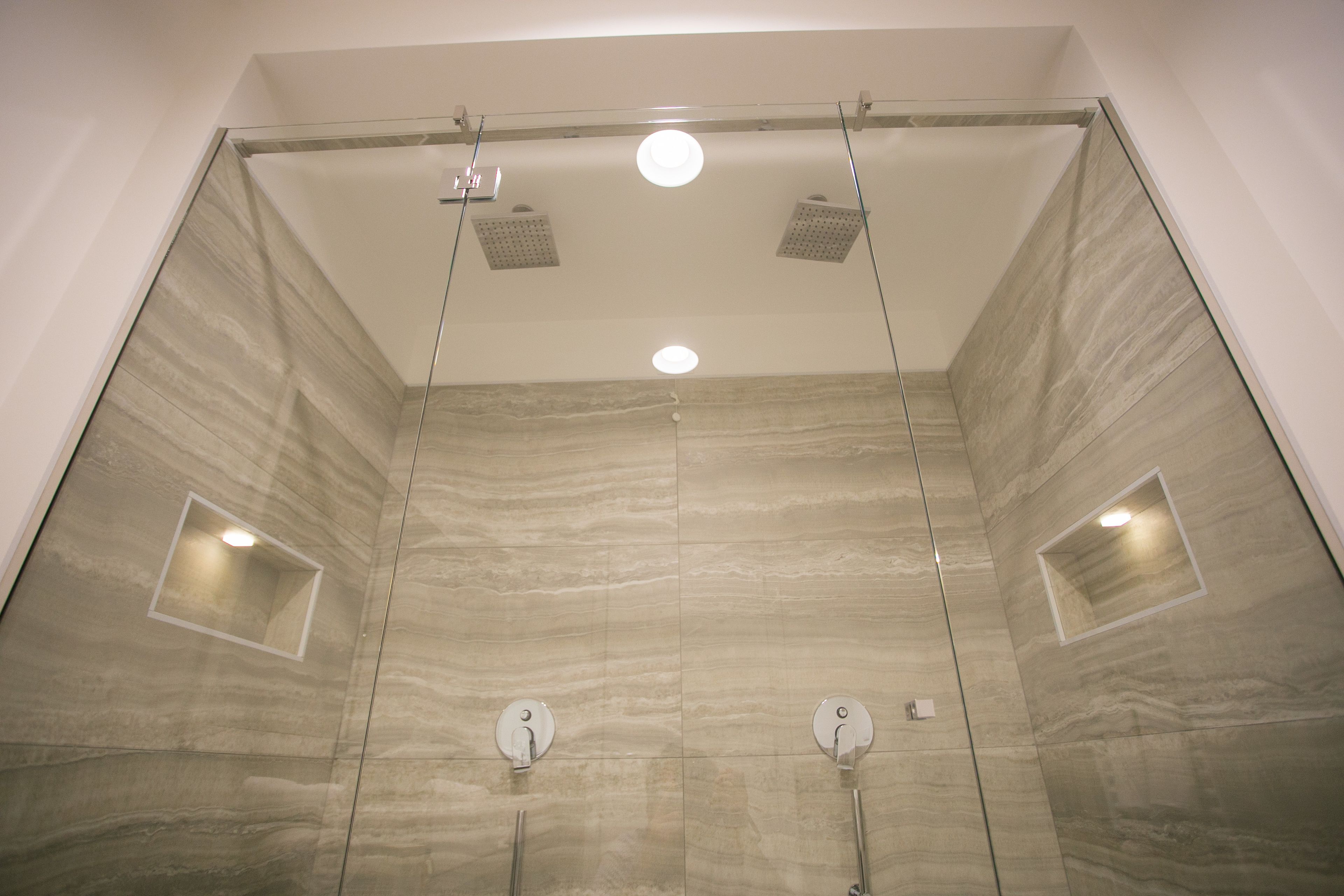 Ducha moderna con cabina de vidrio, dos cabezales de ducha e iluminación empotrada.