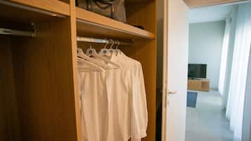 A wooden closet with white shirts hanging on hangers, a handbag on the top shelf, and a door leading to a room with a TV and a wooden cabinet.