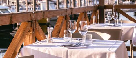 A dining area with tables set for two, overlooking a marina with boats.