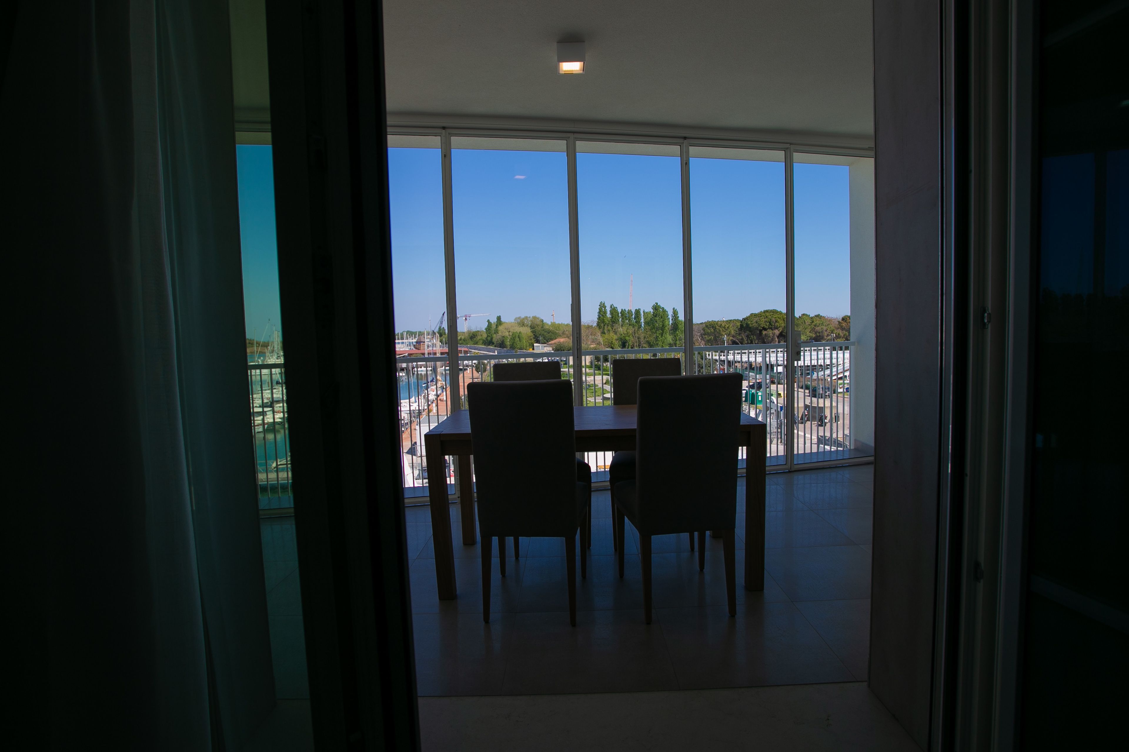 Una habitación con un ventanal grande que ofrece vistas a un paisaje urbano, una mesa de comedor con sillas y vistas a edificios y árboles.