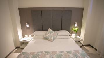A neatly made bed with a patterned bedspread, two bedside tables with lamps, and a nightstand with a vase of flowers.