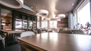 En modern restaurang med ett stort träbord i mitten, flera olika sittgrupper och en bar med utsikt.