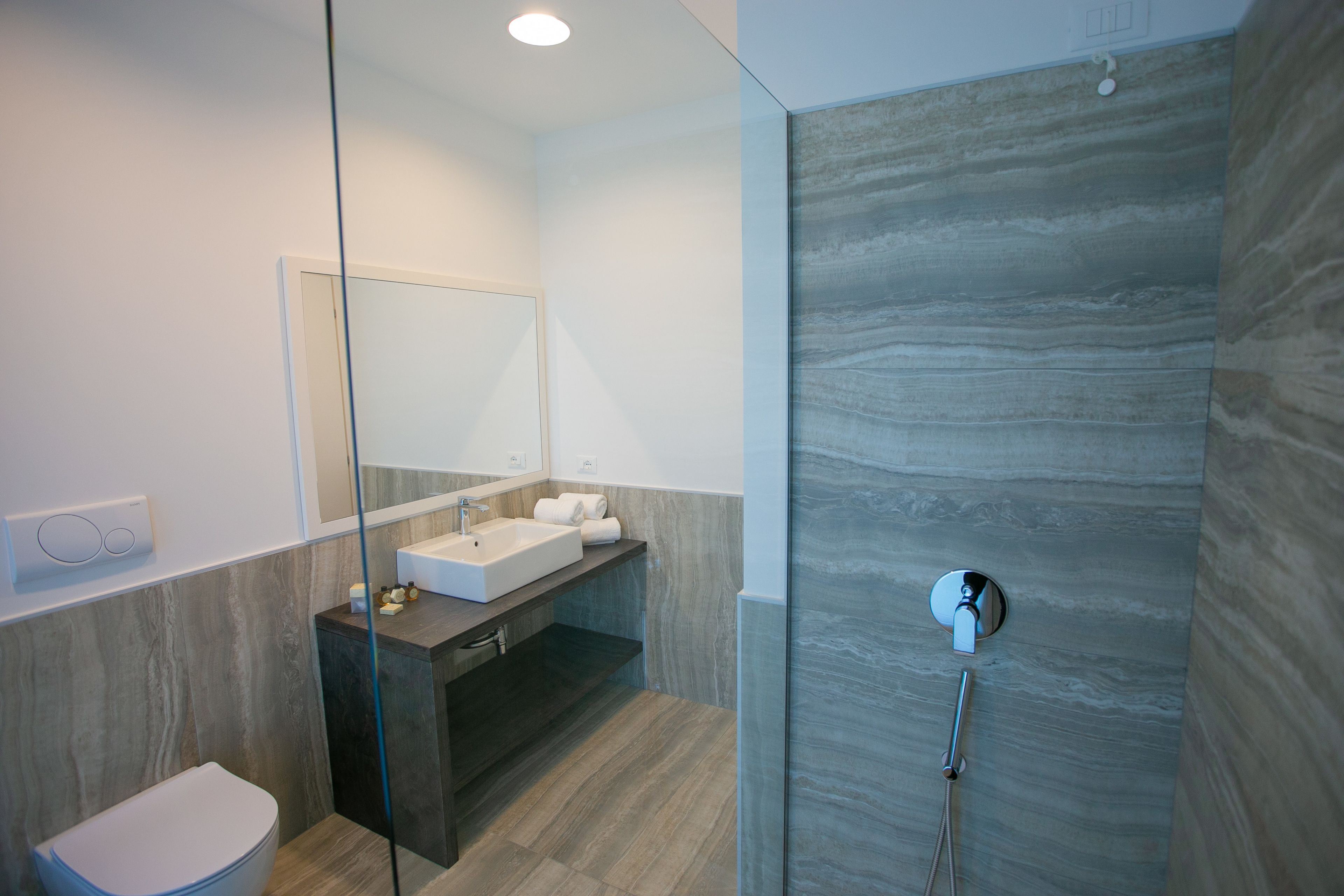 Ein modernes Badezimmer mit einer gläsernen Dusche, einem weißen Waschbecken und einem großen Spiegel.