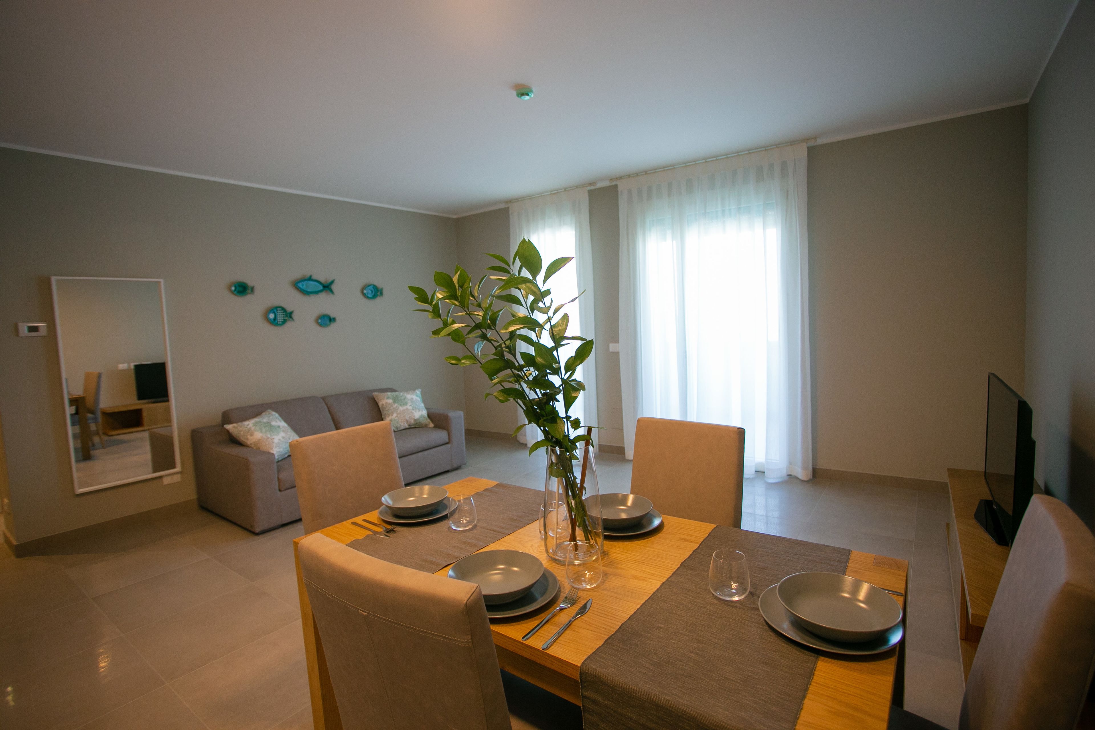 A dining area with a table set for four, a sofa, and a television in a modern living space.