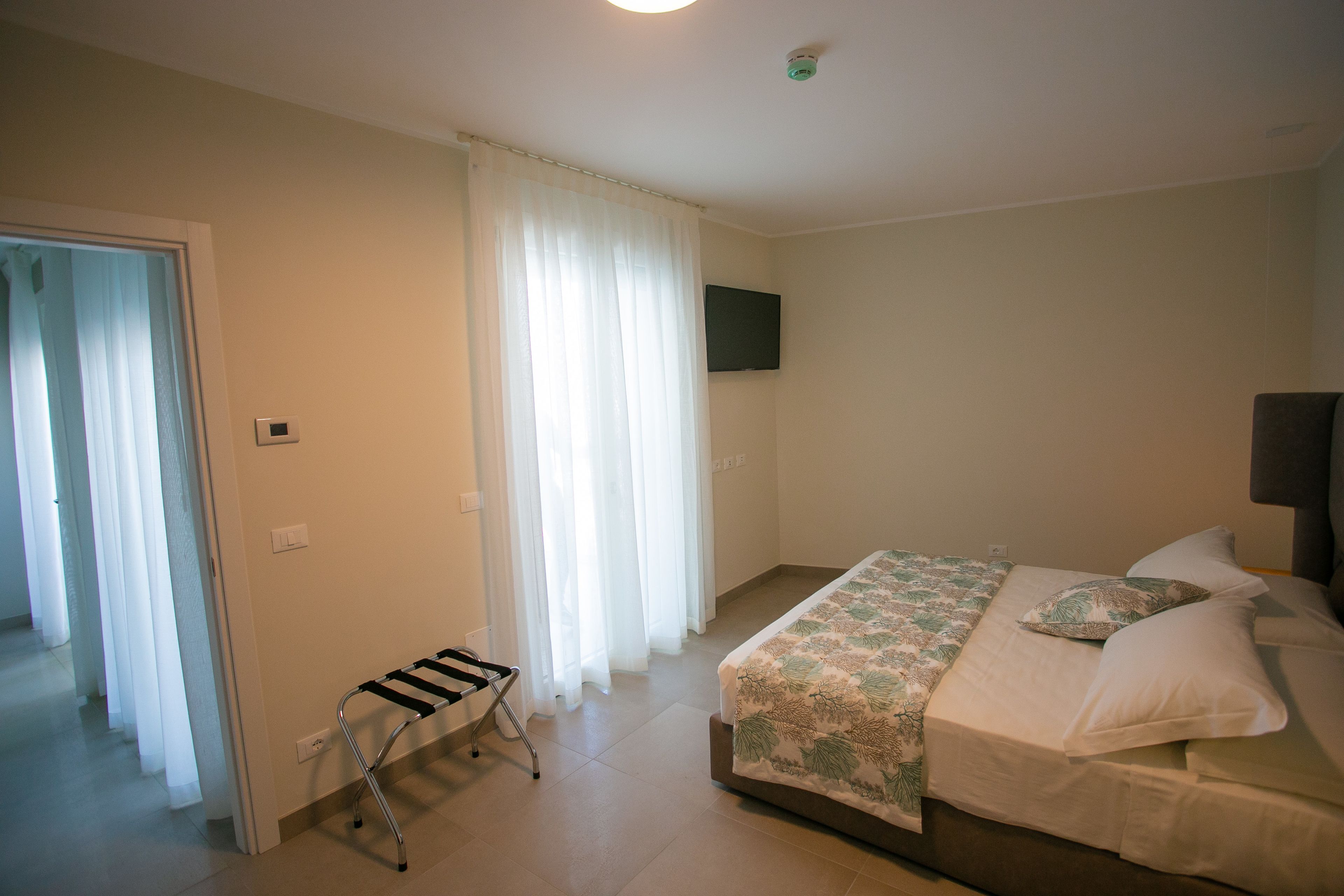 Ein Schlafzimmer mit Bett, einem an der Wand montierten Fernseher und einem fenster mit Vorhängen.