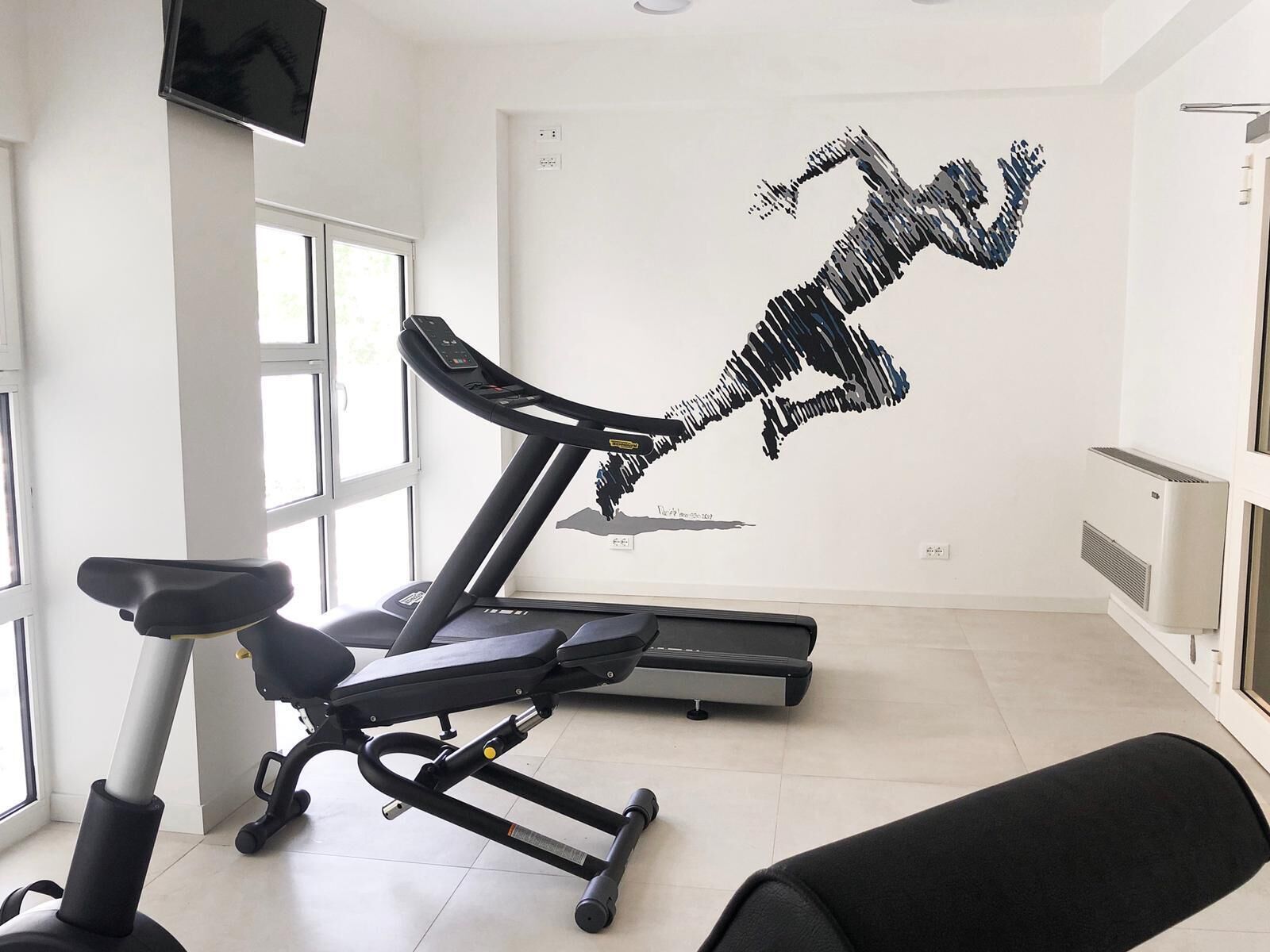 A gym with a treadmill, a stationary bike, and a wall art of a running figure.