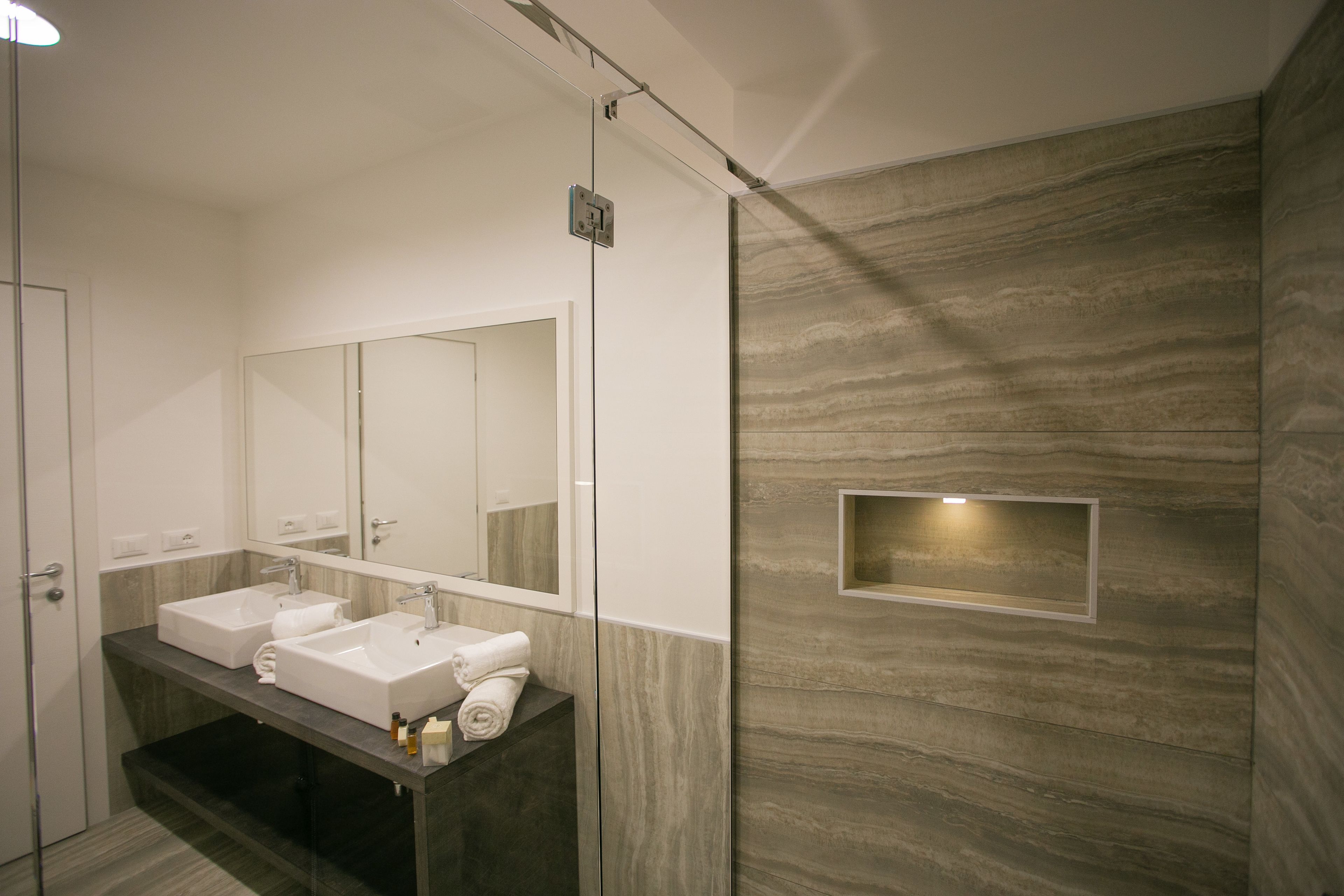 Une salle de bain moderne avec deux vasques, un grand miroir et un meuble-lavabo doté d’un plan de travail foncé.