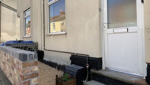 A residential building with a white door, a small front garden with a wooden planter, and a brick wall. - Buccleuch Apartment (Kettering)