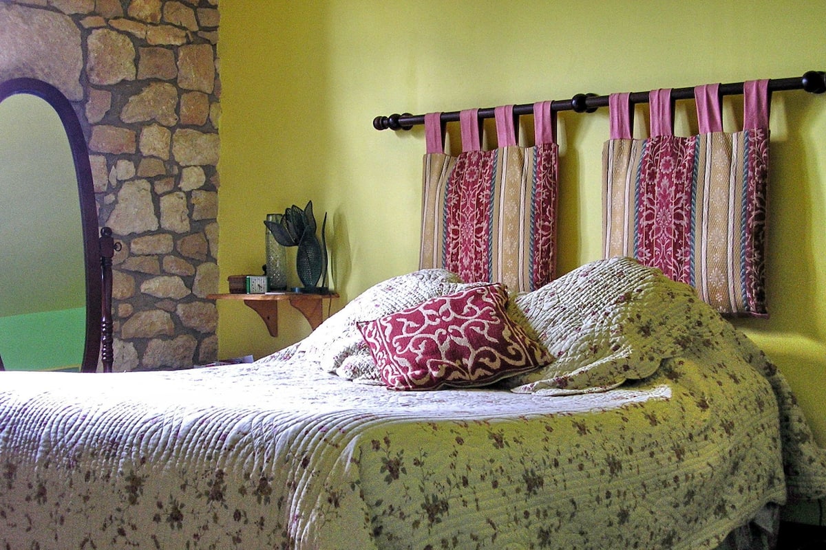 A bed with floral bedding, a stone wall, and a mirror.