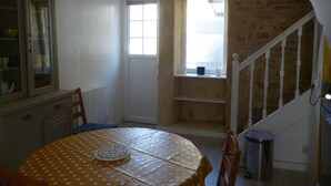 Un comedor con una mesa redonda cubierta con un mantel de lunares, un aparador con puertas de cristal, una ventana y una escalera.