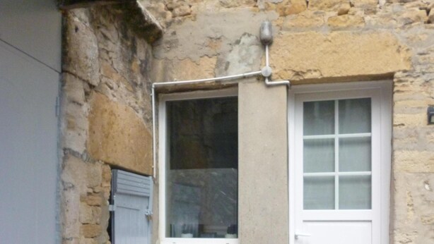 Un edificio de piedra con una ventana pequeña y una puerta, un marco de puerta de metal y un escalón de concreto que lleva a la puerta.