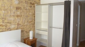 Un dormitorio con pared de piedra, una cama, una mesita de noche, un armario y una cortina.