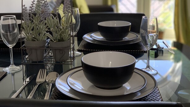 A dining table set with black bowls, plates, and cutlery, accompanied by a potted plant with purple flowers. - Eskdaill Place Apartment (Kettering)