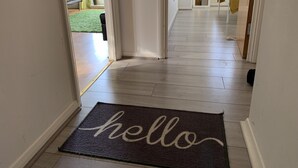 A hallway with a dark doormat spelling "hello" and a wooden floor. - Eskdaill Place Apartment (Kettering)