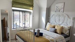 A bedroom with a bed, a window with blinds, a radiator, and a wall-mounted picture. - Eskdaill Place Apartment (Kettering)