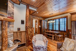A rustic interior with wooden beams, a stone wall, a fireplace, and a dining area with a table and chairs.