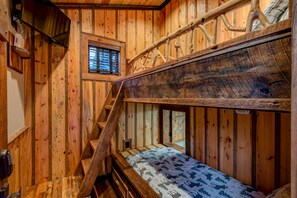 A rustic wooden room with a bunk bed, a small window, and a staircase.