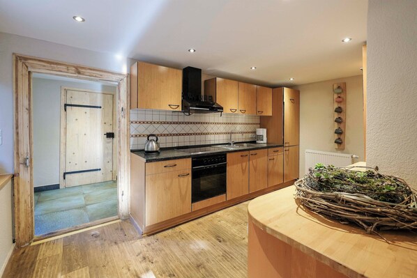 Kitchen features a range hood, kettle, and woven basket on the island, with a door leading to a hallway.