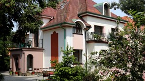 A two-story building with a red-tiled roof, a balcony, and a garden area with potted plants and outdoor furniture. - Hotel Bor (Lhota)