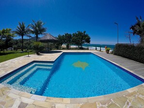 A rectangular swimming pool with clear blue water, surrounded by stone tiles and a wooden deck. - Pousada O Costao do Sol (Balneário Camboriú)