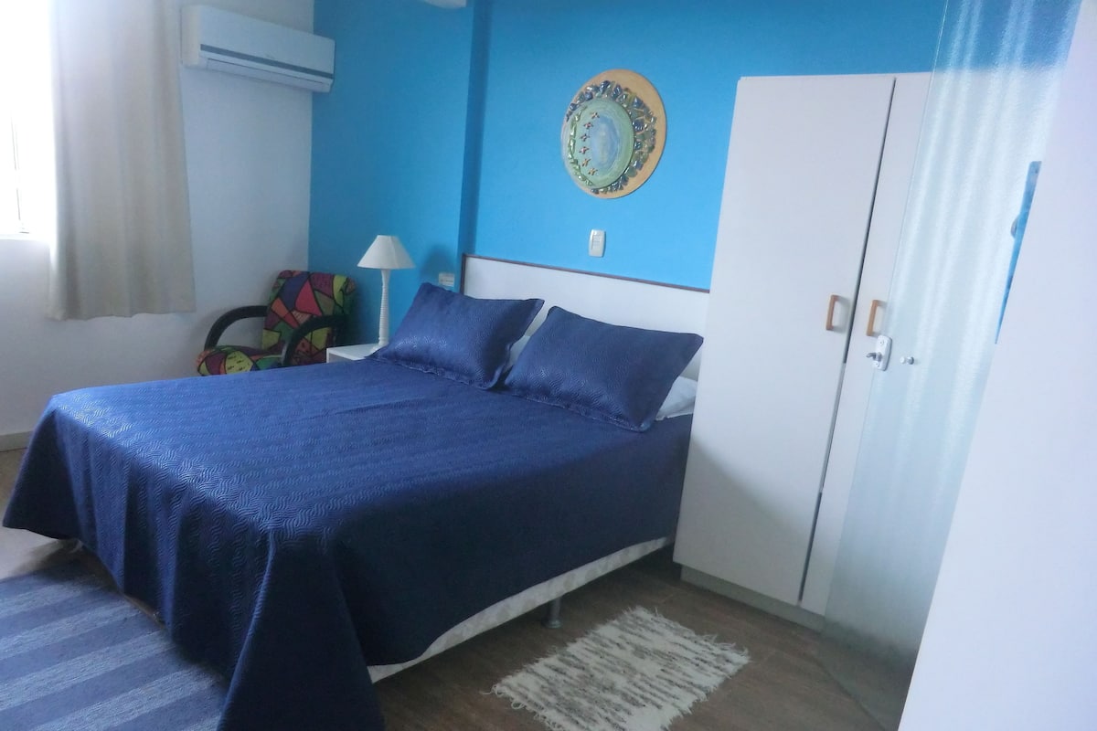 A bedroom with a bed, a wardrobe, a wall clock, and a window with curtains.