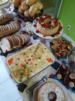 A buffet table with various food items including sliced bread, a layered dish with vegetables, and a cake topped with strawberries. - Pousada O Costao do Sol (Balneário Camboriú)