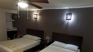 Habitación de hotel con dos camas, un ventilador de techo, una mesita de noche con lámpara y un ventanal con vistas al exterior.