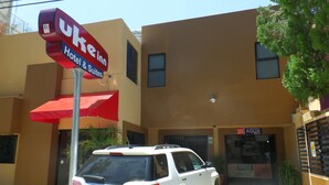 Un SUV GMC blanco estacionado frente a un hotel con un toldo rojo y un letrero que indica que ofrece habitaciones y suites.