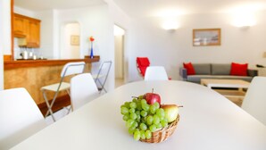 A dining area with a table, chairs, a fruit basket, a kitchen, and a living room with a sofa and pillows. - Club Oceano (Tías)