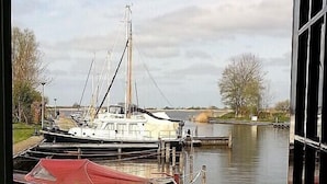 A view of a canal with boats docked, a grassy area in the foreground, and trees in the background.