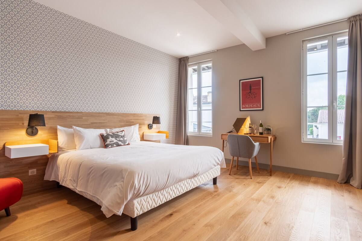 A modern hotel room with a large bed, a desk, and a window with curtains.
