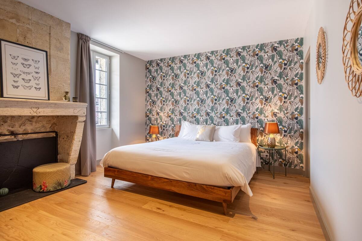 A bedroom with a large bed, a fireplace, and a floral wallpaper.