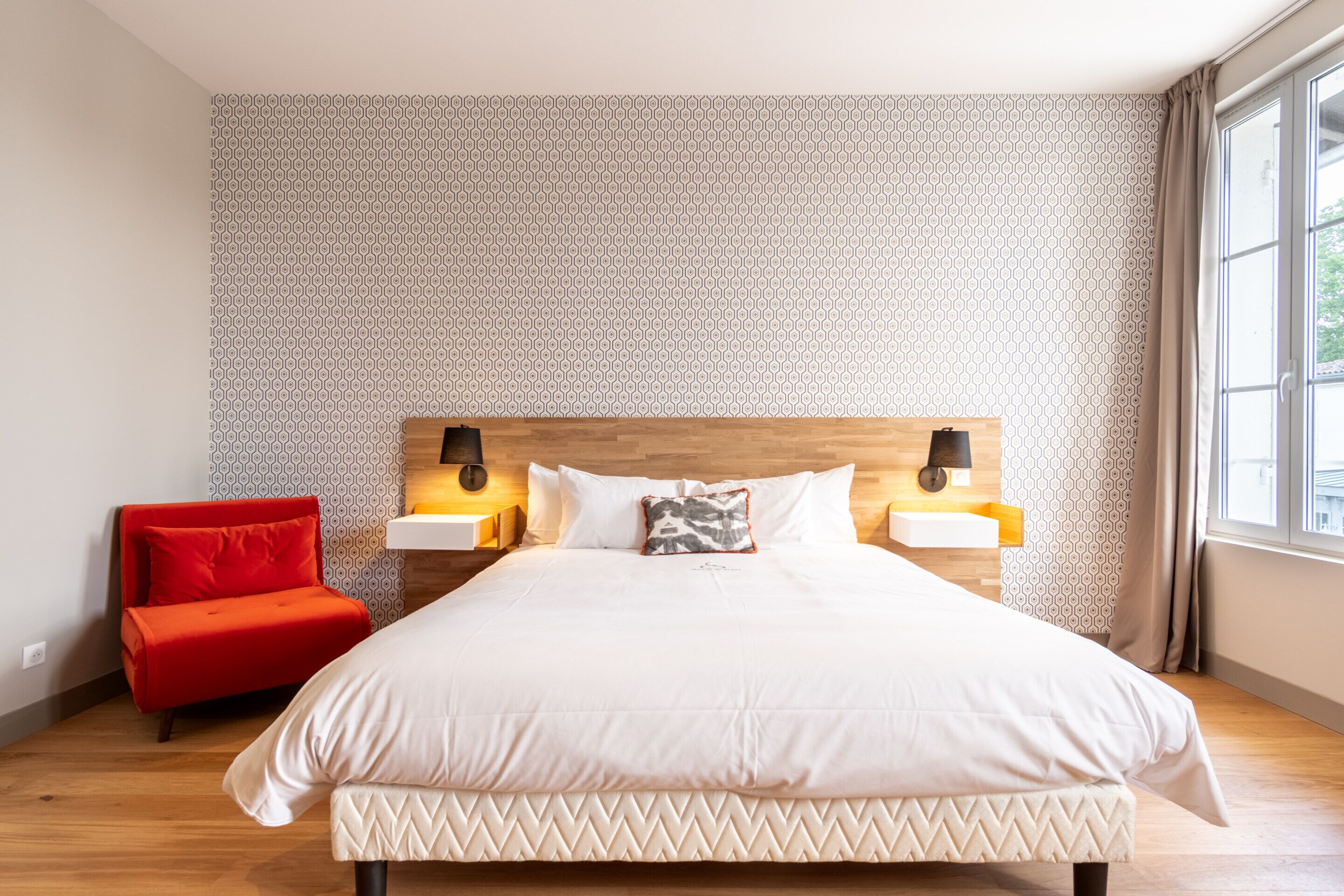 A neatly arranged bedroom with a large bed, a red chair, and two bedside lamps.