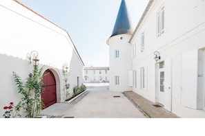 A narrow alleyway with white buildings, a red door, and a blue tower. - Seguin - Chambres Dhôtes (Lignan-de-Bordeaux)