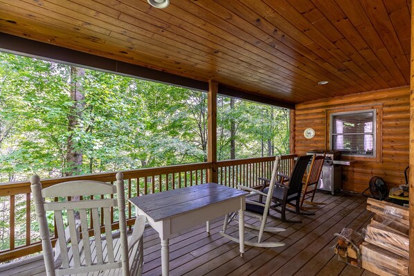 A wooden deck with a table and chairs, a window, and a fan.