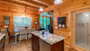 A wooden cabin interior with a kitchen area featuring a granite countertop, a dining table with chairs, and a refrigerator. - Cardinal's Nest- Along Cranberry Creek, great for tubing, kayaking (Elk Park)