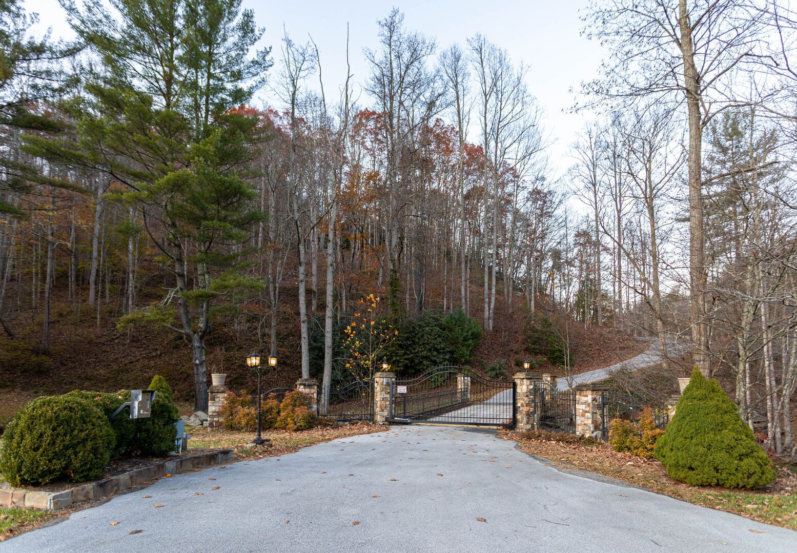 A gated driveway leading to a property surrounded by trees and a stone wall.