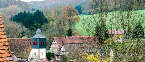 Un pueblo europeo tradicional con una imponente torre de iglesia, rodeado de casas con tejados rojos y un valle verde al fondo.