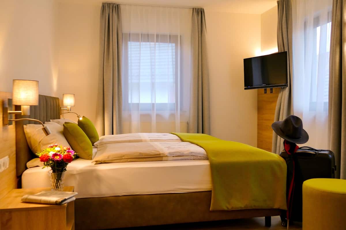 Habitación de hotel con cama, televisor montado en la pared, maleta y un sombrero encima de la maleta.