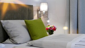 Habitación de hotel con cama, almohada verde, lámpara de pared y un jarrón con flores.
