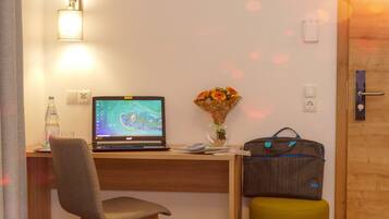 A hotel room with a wooden desk, a laptop, a vase with flowers, a suitcase, and a chair.
