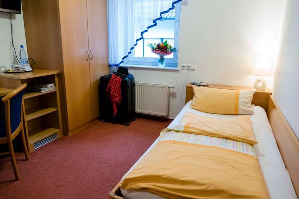 Una habitación de hotel con cama, escritorio con silla, radiador y ventana con cortina.