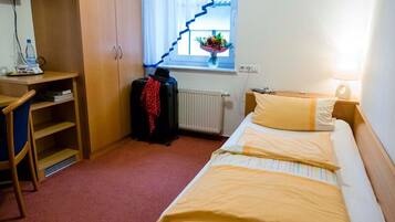 A hotel room with a bed, a desk with a chair, a radiator, and a window with a curtain.