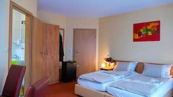 A hotel room with a bed, a chair, a suitcase, a wardrobe, and a painting on the wall.