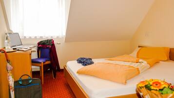 A hotel room with a bed, a desk with a laptop, a chair, a suitcase, and a window with curtains.